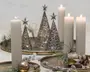 Neutral juledekoration med tændte hvide bloklys, metalliske kegleformede træfigurer med stjerner på toppen, gyldne kugler, grankviste og frostede bær, arrangeret på messingbakker.