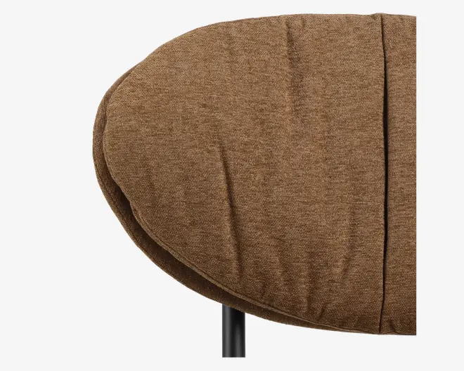 Nærbillede af en rund sædepude betrukket med tekstureret brunt stof. Puden ser tyk og blød ud med diskrete folder og syninger. Kanten er let forhøjet, og et sort metalben er delvist synligt under puden.