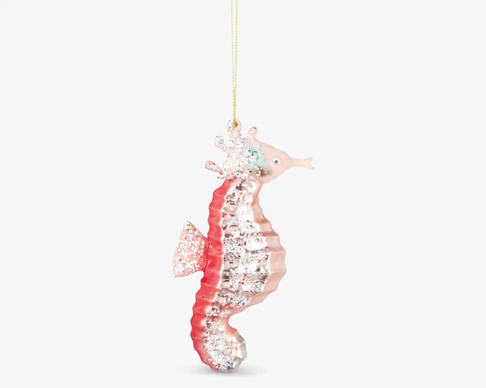 En dekorativ søheste-ornament med glitrende pink og sølvfarver. Kroppen har en tekstureret, ribbet overflade med glimmerdetaljer, og ornamentet hænger i en tynd gylden snor. Søhesten har et detaljeret ansigt og finner samt en skinnende finish, der reflekterer lyset.
