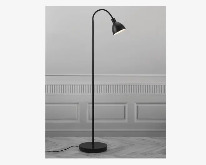 Høj, slank gulvlampe med mat sort finish, rund og stabil fod samt en buet hals, der holder en nedadrettet, kuppelformet skærm. Lampen har et minimalistisk design og en synlig ledning, der går ud fra bunden.