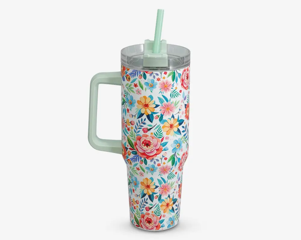 Høj, cylindrisk drikkebæger med stort håndtag og gennemsigtigt låg med et mintgrønt sugerør. Ydersiden er dekoreret med et livligt blomstermønster i nuancer af pink, gul, blå og grøn, hvilket giver et muntert og farverigt udseende.