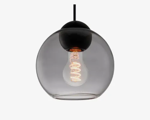 Hængelampe med en klar, rund glasskærm og en synlig glødepære indeni. Pæren har en spiralformet glødetråd, som giver et dekorativt udtryk. Lampen hænger i en sort ledning og har en sort metalfatning i toppen, hvilket giver et moderne og minimalistisk look.