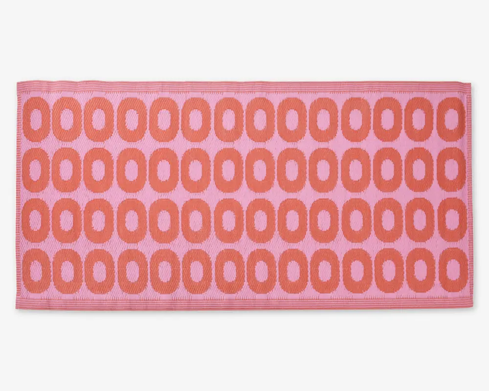 Rektangulært måtte med lyserød baggrund og et gentaget mønster af store, afrundede orange ovaler arrangeret i rækker. Måtten har en tekstureret overflade og en pænt afsluttet kant.