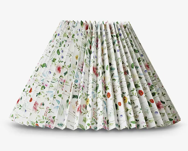 Plisseret lampeskærm med hvid baggrund og et farverigt blomstermønster, der inkluderer forskellige blomster og grønne blade i røde, lilla, gule og blå nuancer. Plisseringen giver en tekstureret og tredimensionel effekt, og det samlede design er friskt og livligt, velegnet til at tilføje et naturinspireret præg til rummet.