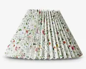 Plisseret lampeskærm med hvid baggrund og et farverigt blomstermønster, der inkluderer forskellige blomster og grønne blade i røde, lilla, gule og blå nuancer. Plisseringen giver en tekstureret og tredimensionel effekt, og det samlede design er friskt og livligt, velegnet til at tilføje et naturinspireret præg til rummet.