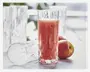 Højt, klart glas med facetslebet diamantmønster, fyldt med en rød frugtdrik. Glasset har en tyk bund og lodrette riller langs siderne, hvilket giver det et tekstureret og elegant udseende. I baggrunden ses et identisk glas, der ligger ned, samt to friske æbler, hvilket antyder, at drikken er lavet af æbler.