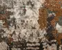Nærbillede af et tekstiler med en abstrakt, slidt mønster. Overfladen har en blanding af jordfarver som brun, beige, grå og strejf af blågrøn. Designet fremstår ujævnt og plettet med områder af både høj og lav luv, hvilket giver en taktil og tredimensionel fornemmelse. Farverne er blandet på en uregelmæssig, organisk måde, hvilket skaber et moderne og kunstnerisk udtryk.