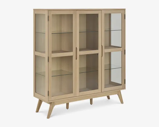 Et vitrineskab i lyst træ med to glaslåger og glaspaneler på siderne, udstyret med tre indvendige glashylder til udstilling. Skabet står på fire skråtstillede ben, hvilket giver det et retro og moderne udtryk. Håndtagene er indbyggede i lågerne for et stilrent look.