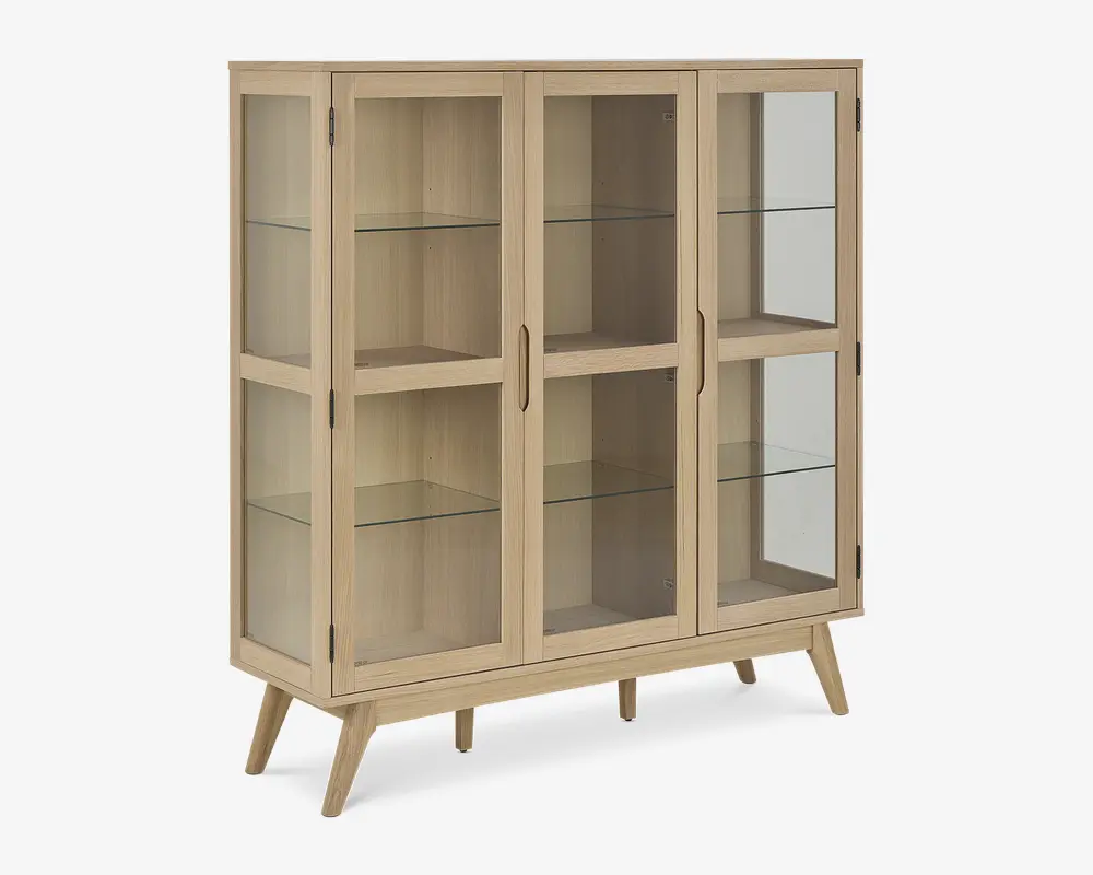 Et vitrineskab i lyst træ med to glaslåger og glaspaneler på siderne, udstyret med tre indvendige glashylder til udstilling. Skabet står på fire skråtstillede ben, hvilket giver det et retro og moderne udtryk. Håndtagene er indbyggede i lågerne for et stilrent look.