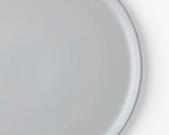 Et nærbillede af en enkel, rund, hvid tallerken med en glat, blank overflade og en let hævet kant. Tallerkenen har et minimalistisk design uden mønstre eller dekorationer.