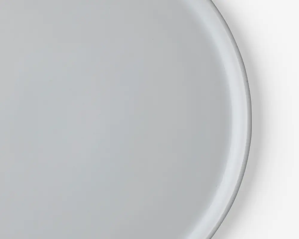 Et nærbillede af en enkel, rund, hvid tallerken med en glat, blank overflade og en let hævet kant. Tallerkenen har et minimalistisk design uden mønstre eller dekorationer.