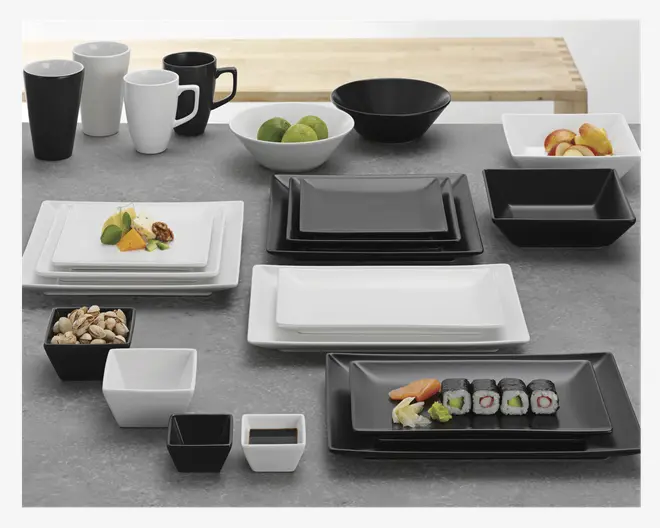 Et moderne stel med en blanding af sorte og hvide dele i et minimalistisk, rektangulært design. Sættet indeholder tallerkener, skåle, krus og små dip-skåle i forskellige størrelser. Tallerkener og skåle har rene, lige kanter og en blank overflade. Nogle af delene er vist med mad, såsom sushi, frugt og nødder, for at illustrere anvendelsen. Stilen er moderne og egner sig både til hverdags- og festbrug.