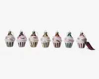 Sæt med seks ornamenter formet som cupcakes, hver med en metallisk bund i forskellige farver (grøn, lilla, guld, sølv, rød, blå) og toppet med en hvid, frosting-lignende dekoration. Hvert ornament har en lille løkke øverst til ophængning, og bundene har lodrette striber. Ornamenterne har en blank finish og et festligt udseende.