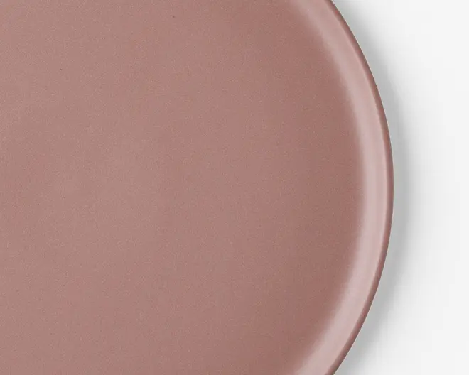 Et nærbillede af en rund tallerken med en glat, mat overflade i en afdæmpet rosa farve. Tallerkenen har en let forhøjet kant og en ensartet overflade, hvilket giver den et moderne og minimalistisk udtryk.