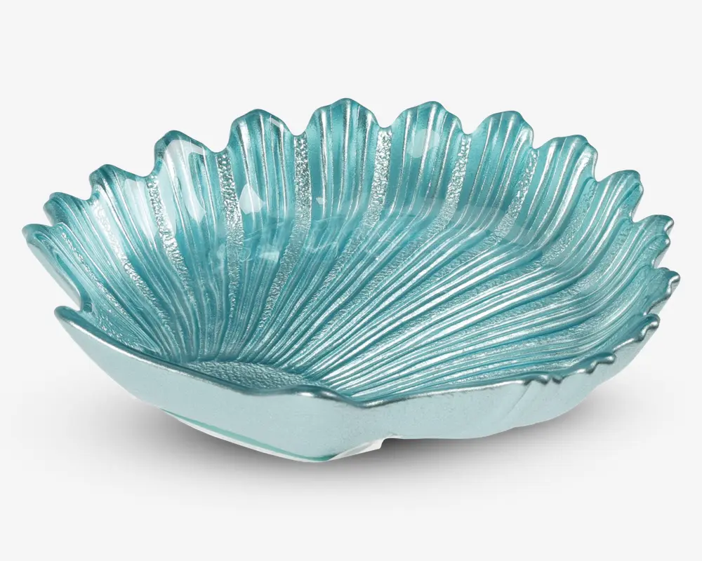 En dekorativ skål lavet af gennemsigtigt turkis glas, formet som et stort blad eller en musling med teksturerede riller og bølgede kanter. Overfladen har en blank finish, og designet har fine detaljer, der efterligner naturlige mønstre, hvilket giver et elegant og kunstnerisk udtryk.