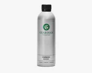 En høj, cylindrisk sølvfarvet flaske med sort skruelåg. Etiket med grønt, cirkulært logo med et 'G' og teksten 'GUARDIAN Furniture Care' i grønt. Under logoet står der 'VARNISH WASH' med sort tekst. Nederst på etiketten står produktnavnet på flere sprog. Flasken har et stilrent, moderne design og ser ud til at være lavet af metal eller metallisk plast.
