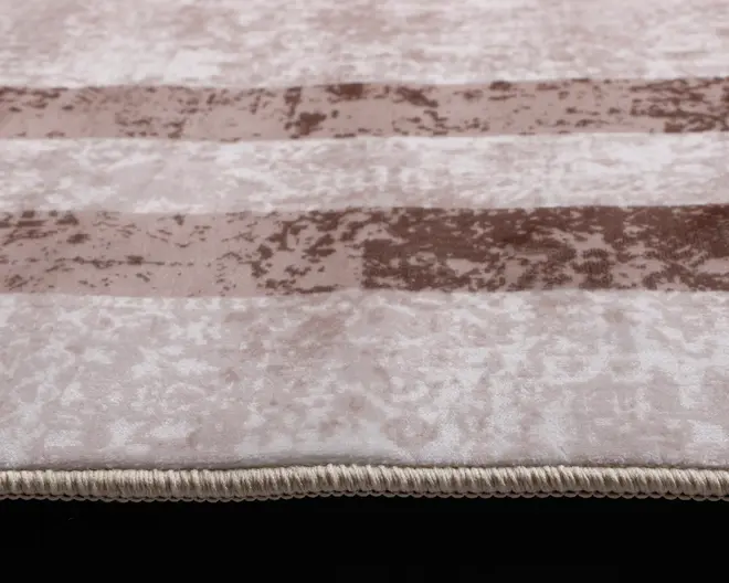 Nærbillede af en tekstureret overflade med skiftevis lyse og mørke beige vandrette striber. Materialet ser blødt og fløjlsagtigt ud med et diskret marmoreret mønster. Kanten er afsluttet med en tæt vævet, lysefarvet kant for holdbarhed og et pænt udseende.