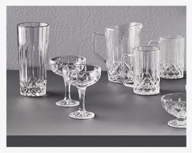 Et sæt klart glas med klassisk facetslebet krystaldesign og indviklede geometriske mønstre. Sættet indeholder et højt glas, to coupeglas med korte stilke, en kande med hank og hældetud, to store krus med hank samt en lille dessert- eller cocktailskål. Alle dele har en facetslebet bund, der reflekterer lyset og giver et elegant og tidløst udtryk.