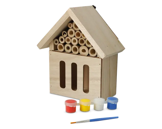 En husformet struktur af træ med skråt tag, der har flere hule bambusrør arrangeret under taget og tre lodrette åbninger på frontpanelet. Træet er ubehandlet, hvilket gør det muligt at dekorere. Foran strukturen ligger fire små malerbøtter i rød, gul, hvid og blå samt en pensel, hvilket viser, at produktet kan males og personliggøres.