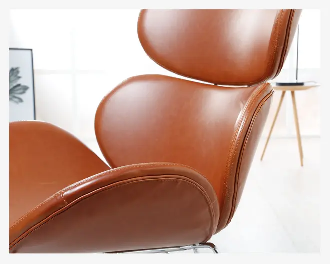 Nærbillede af en moderne stol med glat, lysebrun læderpolstring. Stolen har ergonomisk formede puder på sæde, ryg og hovedstøtte med synlige syninger langs kanterne. Læderet har en let glans, og polstringen ser tyk og komfortabel ud. Stellet er delvist synligt og ser ud til at være af metal, hvilket giver et moderne udtryk.