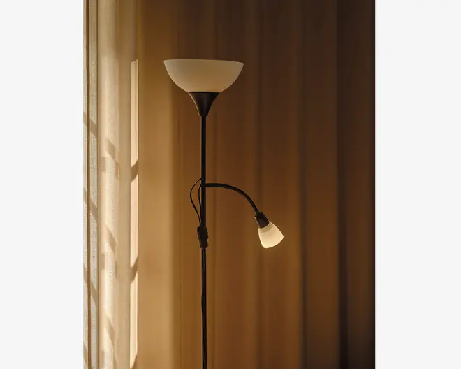 Høj standerlampe med sort metalstang og to lyskilder: en opadrettet, skålformet hovedlampe øverst og en mindre, justerbar læselampe fastgjort til stangen. Begge lamper har matterede, hvide glasskærme. Læselampen sidder på en fleksibel arm, så den nemt kan rettes.