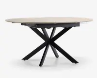 Et moderne bord med en lys, rund bordplade med glat overflade. Bordets ben er lavet af sort metal og er arrangeret i et markant krydset stjernemønster, hvilket giver både stabilitet og et moderne udtryk.