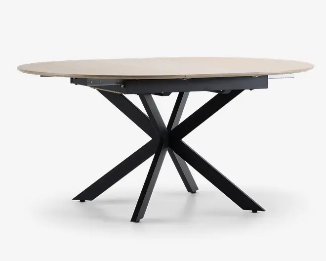 Et moderne bord med en lys, rund bordplade med glat overflade. Bordets ben er lavet af sort metal og er arrangeret i et markant krydset stjernemønster, hvilket giver både stabilitet og et moderne udtryk.