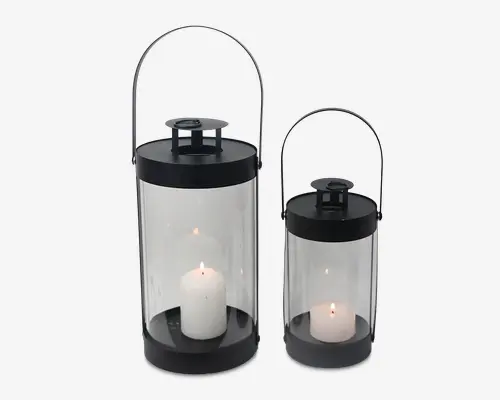 Sæt med to cylindriske lanterner med sorte metal-låg og -bunde samt klare glassider. Hver lanterne har et solidt, buet håndtag, der gør dem nemme at bære eller hænge op. Indeni er der hvide bloklys, ét i hver lanterne, som giver et varmt og hyggeligt lys. Designet er moderne og minimalistisk, velegnet til både indendørs og udendørs brug.
