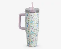 Høj, isoleret drikkebæger med et pastelfarvet blomsterprint, der viser lyserøde, blå og gule blomster på hvid baggrund. Bægeret har et stort, solidt lyserødt håndtag og et matchende lyserødt låg med opklappeligt sugerør. Det gennemsigtige låg slutter tæt, og designet er både funktionelt og dekorativt, velegnet til at holde drikkevarer varme eller kolde.