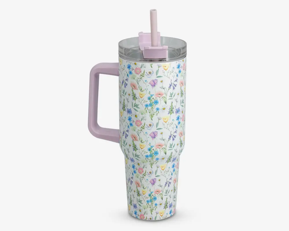 Høj, isoleret drikkebæger med et pastelfarvet blomsterprint, der viser lyserøde, blå og gule blomster på hvid baggrund. Bægeret har et stort, solidt lyserødt håndtag og et matchende lyserødt låg med opklappeligt sugerør. Det gennemsigtige låg slutter tæt, og designet er både funktionelt og dekorativt, velegnet til at holde drikkevarer varme eller kolde.