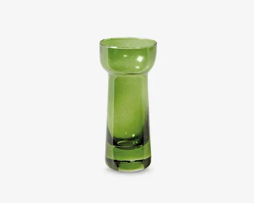 Højt, cylindrisk glas i grøn med en tyk, solid bund og en bred, afrundet kant. Glasset har en glat, blank overflade og et moderne, minimalistisk design. Den grønne farve er gennemsigtig, så lyset kan skinne igennem og fremhæve glassets tykkelse.