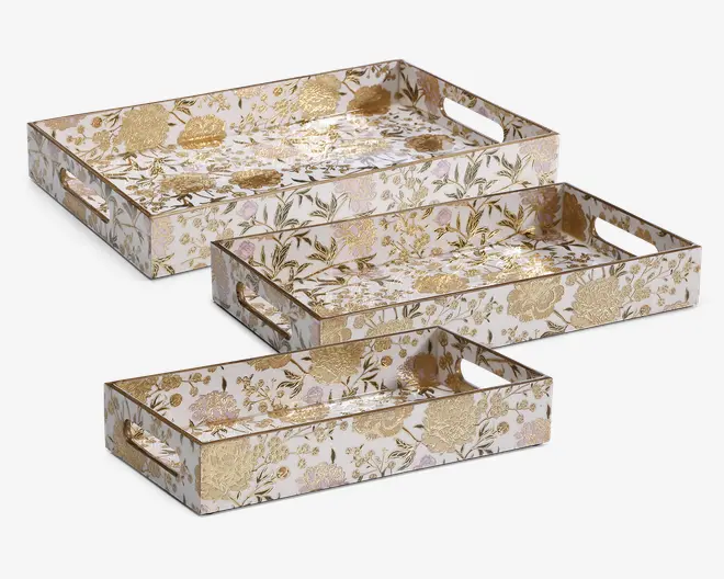 Sæt med tre rektangulære bakker i forskellige størrelser, hver med en blank overflade og et detaljeret blomstermønster i guld og bløde pastelfarver. Bakkerne har høje kanter og indbyggede håndtag på de korte sider for nem transport. Blomstermotivet dækker både inderside og yderside, hvilket giver et sammenhængende og elegant udtryk.