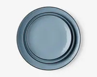 Sæt med tre runde tallerkener i forskellige størrelser, alle med en glat, blank lyseblå overflade og en diskret forhøjet kant. Tallerkenerne kan stables pænt oven i hinanden og har et moderne, minimalistisk design, der passer til både hverdagsbrug og særlige lejligheder.