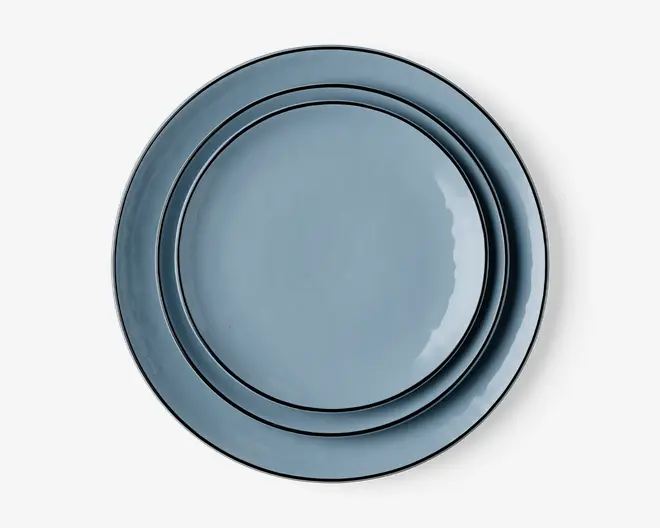 Sæt med tre runde tallerkener i forskellige størrelser, alle med en glat, blank lyseblå overflade og en diskret forhøjet kant. Tallerkenerne kan stables pænt oven i hinanden og har et moderne, minimalistisk design, der passer til både hverdagsbrug og særlige lejligheder.