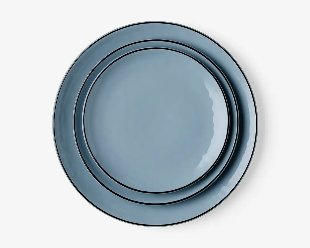 Sæt med tre runde tallerkener i forskellige størrelser, alle med en glat, blank lyseblå overflade og en diskret forhøjet kant. Tallerkenerne kan stables pænt oven i hinanden og har et moderne, minimalistisk design, der passer til både hverdagsbrug og særlige lejligheder.