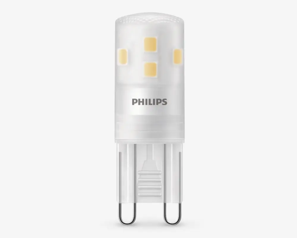 Kompakt LED-pære med cylindrisk form, mat hvid overflade og flere små gule LED-chips placeret rundt om den øverste del. Pæren har en G9 stiftfatning, der gør den nem at montere i kompatible armaturer. Philips-logoet er trykt på siden, hvilket angiver mærket. Designet til energieffektivitet og lang levetid.