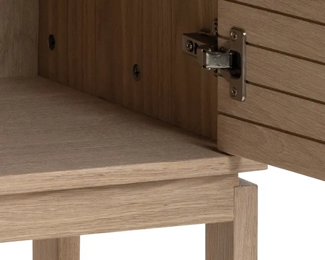 Nærbillede af et skab i lyst træ med åben låge, der viser den indvendige hylde og metalhængsel. Lågen har vandrette riller for ekstra struktur, og skabet har en naturlig træstruktur.