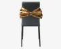 En moderne stol med en elegant, mat sort finish og slanke, lige ben. Det mest iøjnefaldende træk er en stor, metallisk guldfarvet sløjfe, der er fastgjort til ryglænet og giver stolen et markant og luksuriøst udseende. Sløjfen er blank og formet, hvilket tilføjer et dekorativt og opsigtsvækkende element til det ellers minimalistiske design.