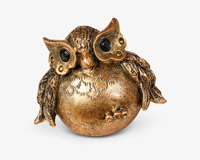 En dekorativ uglefigur lavet af metal med en gylden finish. Uglen har en rund, glat krop med indgraverede fjerdetaljer og store, sorte, blanke øjne. Vingerne er teksturerede og strakt let ud til siderne, og der er små skulpturerede bær nær basen. Det samlede design er finurligt og elegant, velegnet til boligindretning.