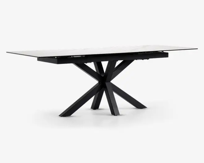 Rektangulært bord med en glat, hvid marmoreret eller marmorlignende bordplade og en markant sort metalbase. Basen har et kantet, stjerneformet design med flere ben, der stråler ud fra et centralt punkt, hvilket giver både stabilitet og et moderne, skulpturelt udtryk. Bordet har rene linjer og en nutidig stil.