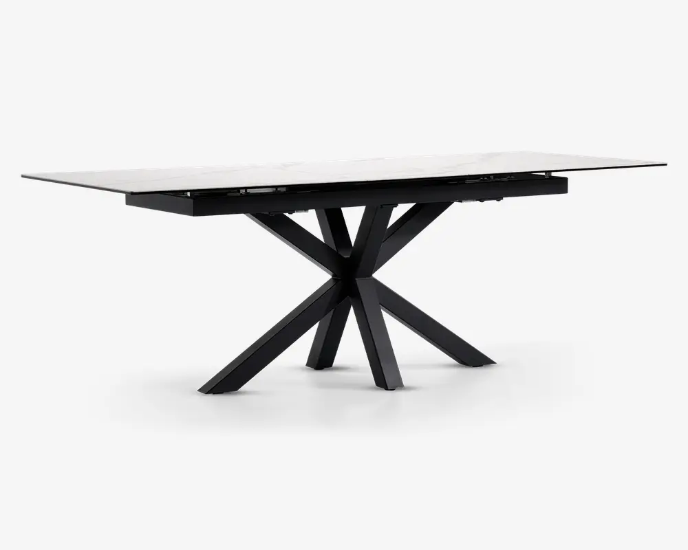 Rektangulært bord med en glat, hvid marmoreret eller marmorlignende bordplade og en markant sort metalbase. Basen har et kantet, stjerneformet design med flere ben, der stråler ud fra et centralt punkt, hvilket giver både stabilitet og et moderne, skulpturelt udtryk. Bordet har rene linjer og en nutidig stil.