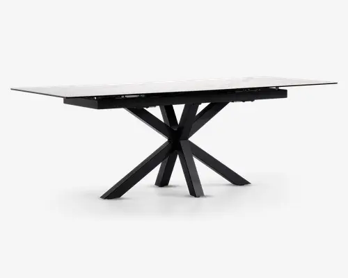 Rektangulært bord med en glat, hvid marmoreret eller marmorlignende bordplade og en markant sort metalbase. Basen har et kantet, stjerneformet design med flere ben, der stråler ud fra et centralt punkt, hvilket giver både stabilitet og et moderne, skulpturelt udtryk. Bordet har rene linjer og en nutidig stil.