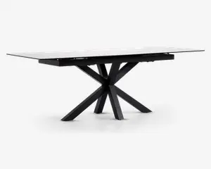 Rektangulært bord med en glat, hvid marmoreret eller marmorlignende bordplade og en markant sort metalbase. Basen har et kantet, stjerneformet design med flere ben, der stråler ud fra et centralt punkt, hvilket giver både stabilitet og et moderne, skulpturelt udtryk. Bordet har rene linjer og en nutidig stil.