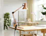 Justerbar skrivebordslampe med kobberfarvet metalskærm og arm, sorte metalled og en klemmefod til fastgørelse på bordkanten. Lampen har et moderne, industrielt design og en fleksibel arm, der gør det nemt at justere lysets placering. Strømkablet er synligt og hænger ned fra lampens base.