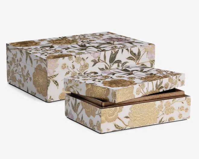 Sæt med to rektangulære æsker med matchende blomsterdesign i guld, grønne og beige nuancer på hvid baggrund. Æskerne har indviklede, prægede guldfarvede blomster og bladmønstre, hvilket giver dem et luksuriøst og elegant udseende. Den ene æske er lidt større end den anden, og den mindre æske vises med låget delvist åbent, så man kan se en brun indvendig foring.