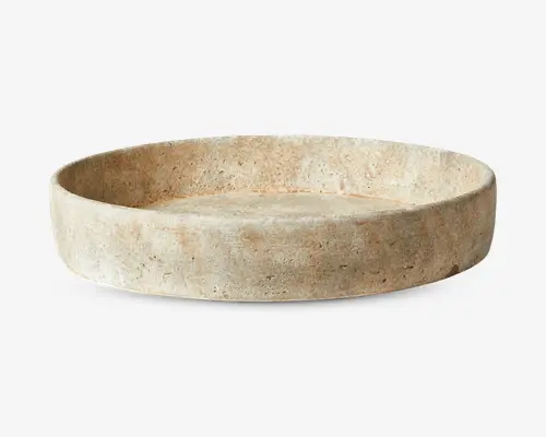 Rund, lav bakke lavet af naturlig beige sten med en tekstureret, let ru overflade. Bakken har tykke, lige sider og en flad bund, og viser diskrete farve- og mønstervariationer, som er typiske for stenmateriel. Udtrykket er rustikt og minimalistisk.