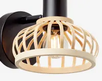 Væghængt lampe med en rund sort base og en dekorativ åben lampeskærm lavet af lyse trælameller. Pæren er synlig gennem den trælignende skærm, hvilket giver et moderne og naturligt udtryk. Lampen kombinerer metal og træ for et nutidigt design.