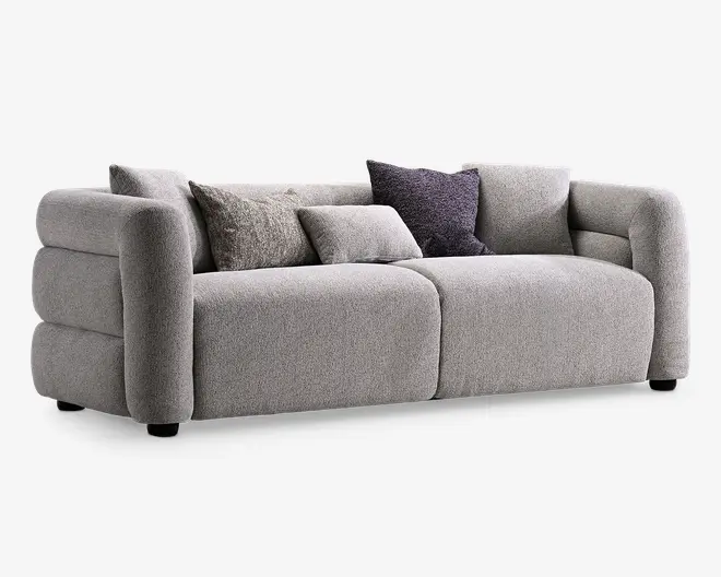 Stor lysegrå polstret sofa med afrundede armlæn, dybe sædehynder og fem løse ryghynder i forskellige grå nuancer, inklusive en mørk pyntepude.