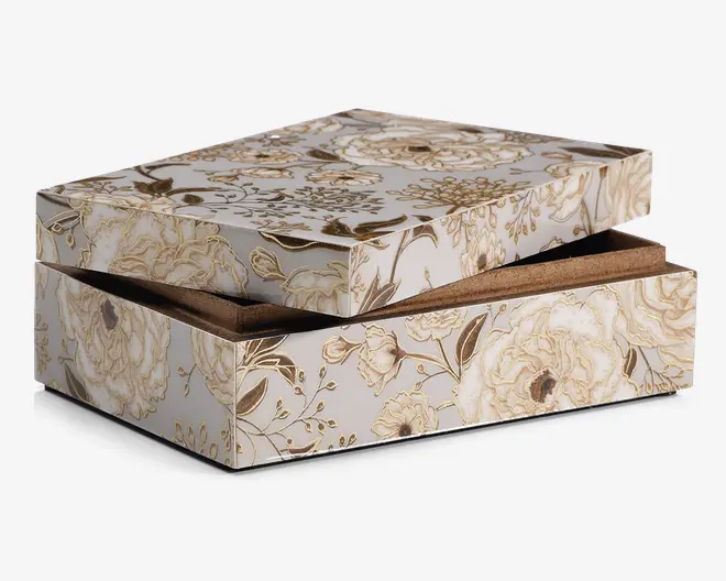 Rektangulær æske med hængslet låg, dekoreret med et elegant blomstermønster i gyldne og cremefarvede nuancer på hvid baggrund. Æsken har en glat, blank overflade, og blomstermotivet dækker alle synlige flader, hvilket giver et sofistikeret og dekorativt udtryk. Indersiden ser ud til at være foret med et blødt, brunt materiale for ekstra beskyttelse.