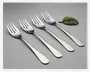 Sæt med fire polerede gafler i rustfrit stål med et enkelt, moderne design. Hver gaffel har tre brede tænder og et glat, let buet skaft med afrundet ende. Overfladen er blank og reflekterende, og skaftet er uden dekoration eller mønster. Gaflerne ligger på række på en ensfarvet, lysegrå baggrund, og øverst til højre ligger et enkelt grønt blad som dekoration.